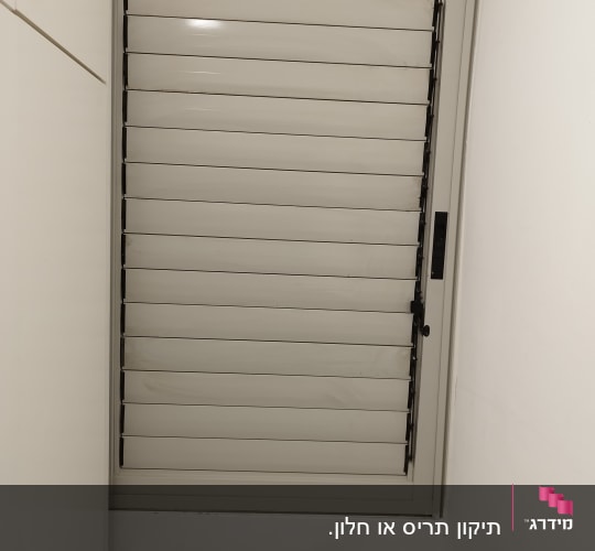 תריסים סגורים בצבע אפור על חלון קיר לבן